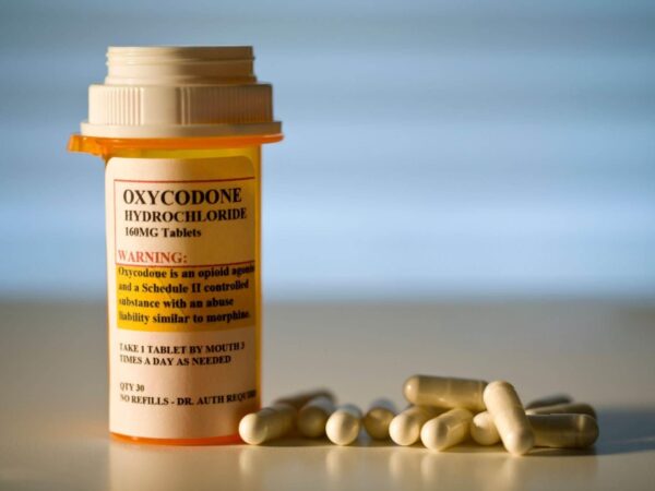 A close-up image of prescription-labeled Oxycodone tablets in a pill bottle, with a glass of water beside it. Buy Oxycodone Online.
