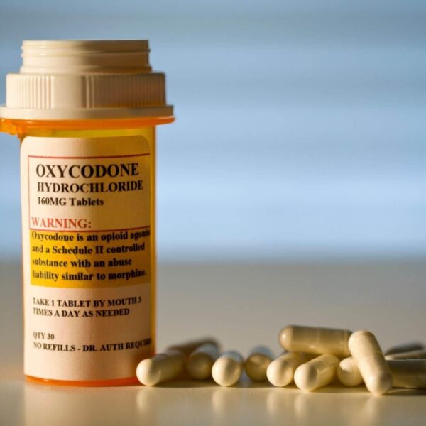 A close-up image of prescription-labeled Oxycodone tablets in a pill bottle, with a glass of water beside it. Buy Oxycodone Online.