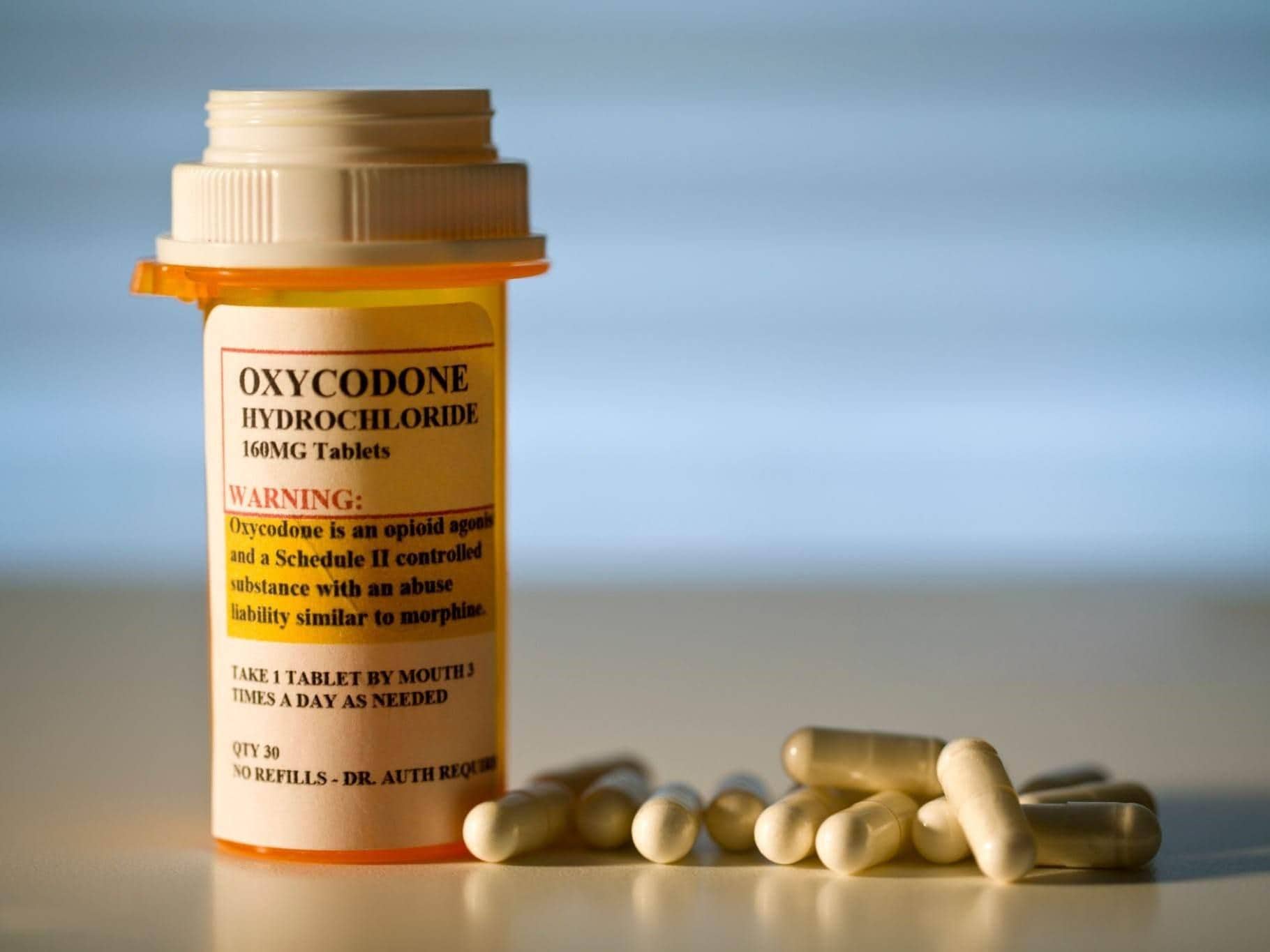A close-up image of prescription-labeled Oxycodone tablets in a pill bottle, with a glass of water beside it. Buy Oxycodone Online.
