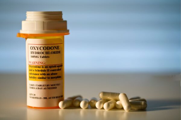 A close-up image of prescription-labeled Oxycodone tablets in a pill bottle, with a glass of water beside it. Buy Oxycodone Online.