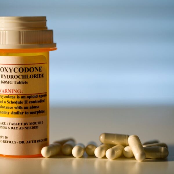 A close-up image of prescription-labeled Oxycodone tablets in a pill bottle, with a glass of water beside it. Buy Oxycodone Online.